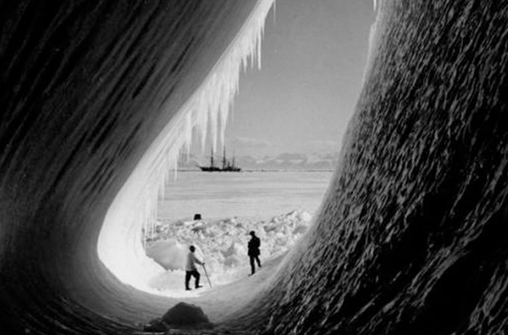 photo de deux scientifique britanniques dans la cavité d'un glacier avec le bateau en arrière plan