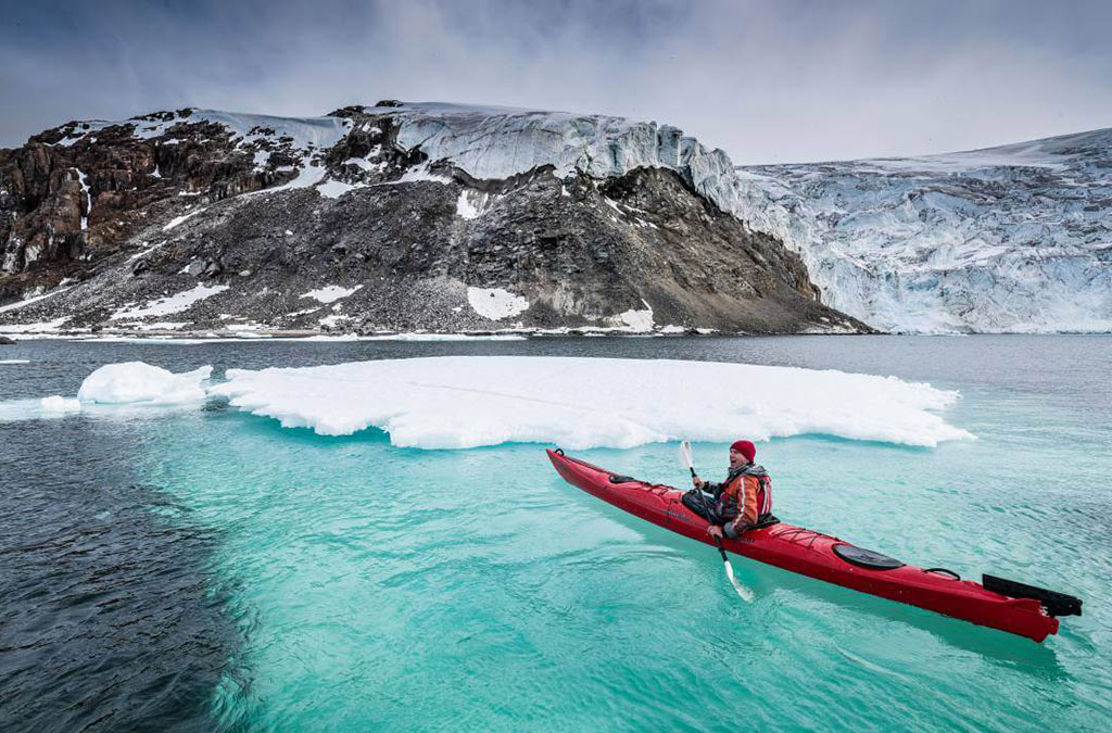 un kayak devant un iceberg dont on voit la partie immergée