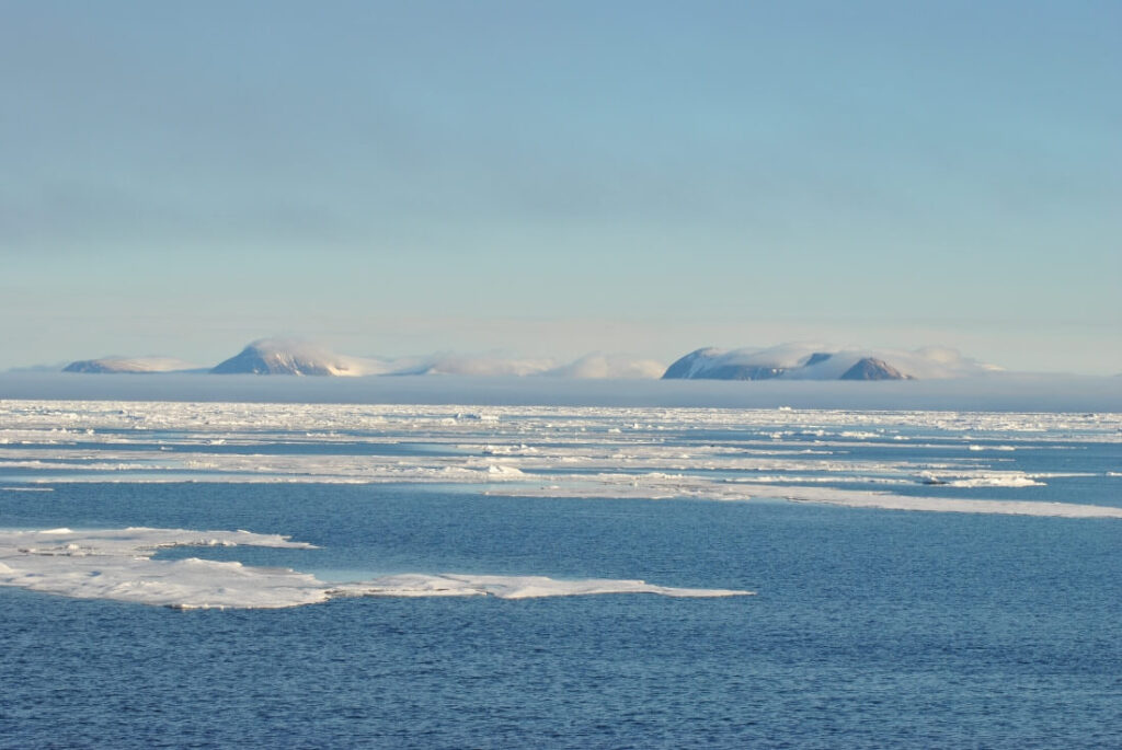 une mer de glace sous le soleil avec la chaine de montagne du Spitzberg en fond de tableau