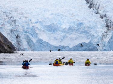 des kayak pagaient au pied d'un glacier
